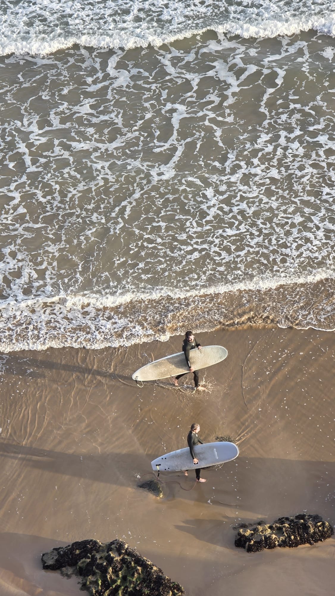 Two surfers walking along the Imsouane shoreline with Atlantic foam